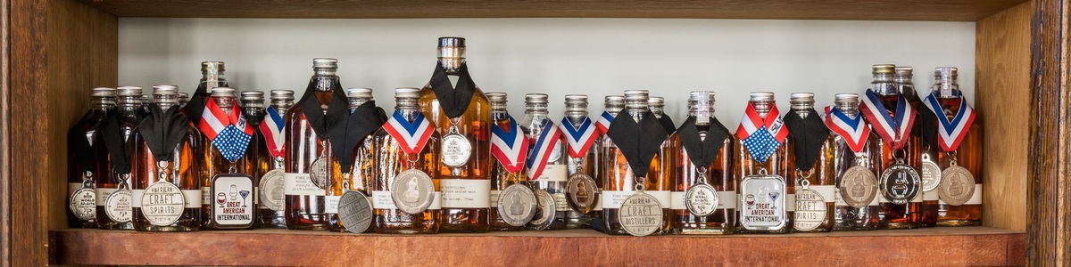 Kings County Distillery whiskey bottles displaying competition medals on a wooden shelf.